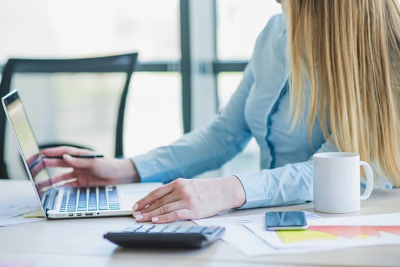 jeune femme travaillant sur laptop avec calculette, mug et téléphone