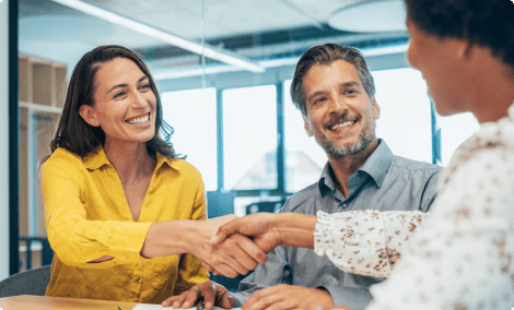 Trois personnes souriantes se serrant la main dans un environnement de bureau, symbolisant une collaboration.