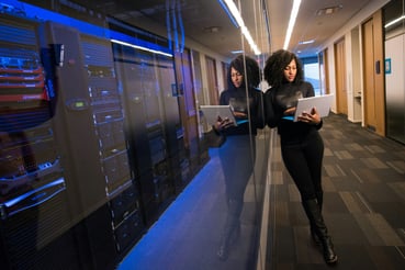 Femme gérant les infrastructure sécurisées depuis son laptop, devant des rangées de serveurs