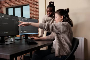 Deux jeunes développeuses concentrées sur un ordinateur, en train d'échanger sur du code.